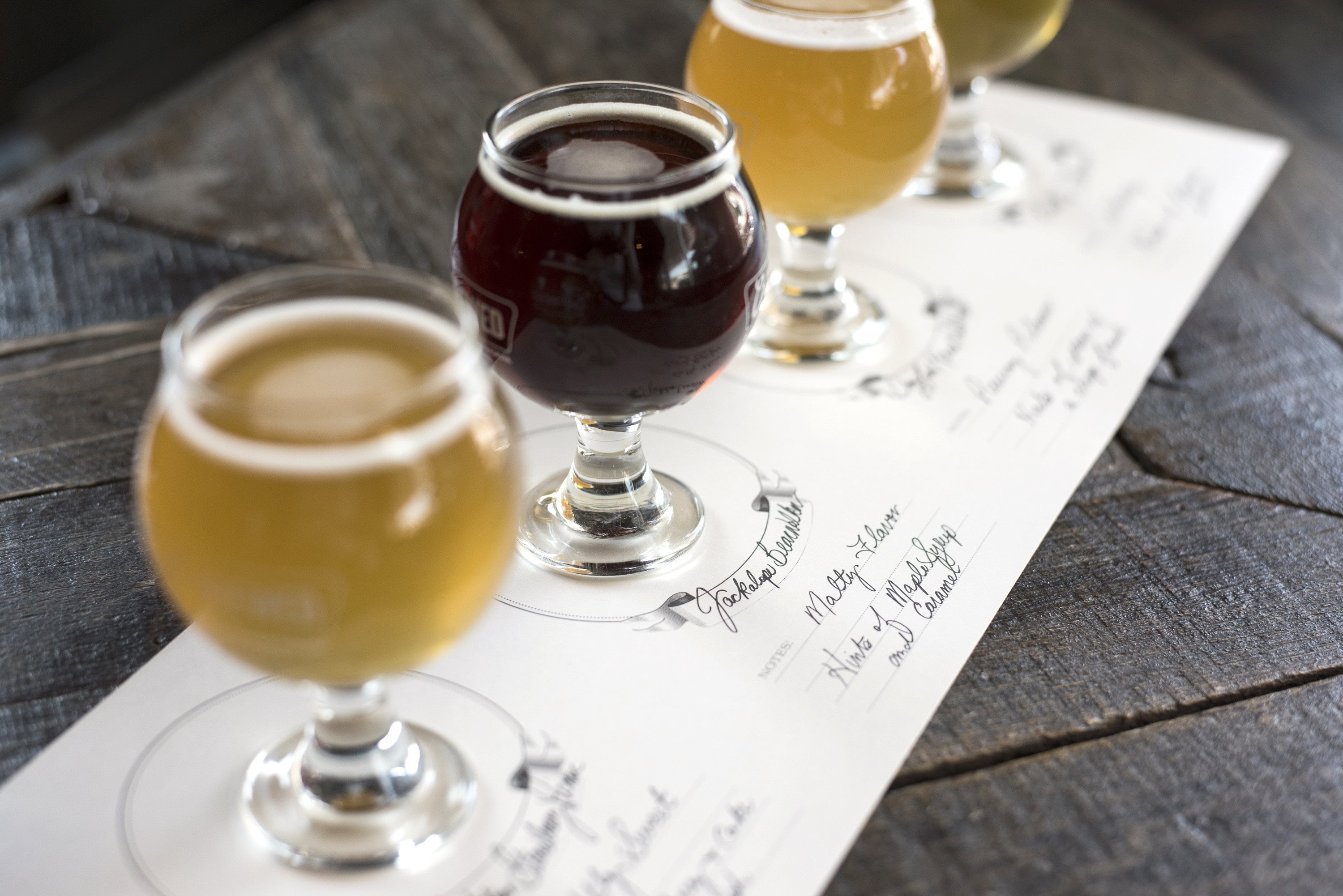 A flight of four different beers set out and labeled on the four spots of a Tasting Paper.