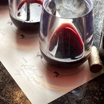 Close-up of a flight of red wines, set out and labeled on a Hester &amp; Cook Tasting Paper.