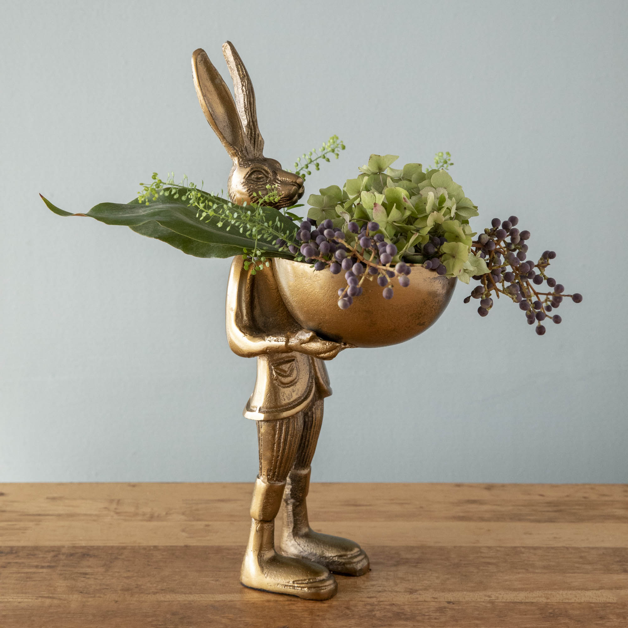 A well-dressed Accent Decor standing hare holding a round dish of plants, called the Hare Dishstand.