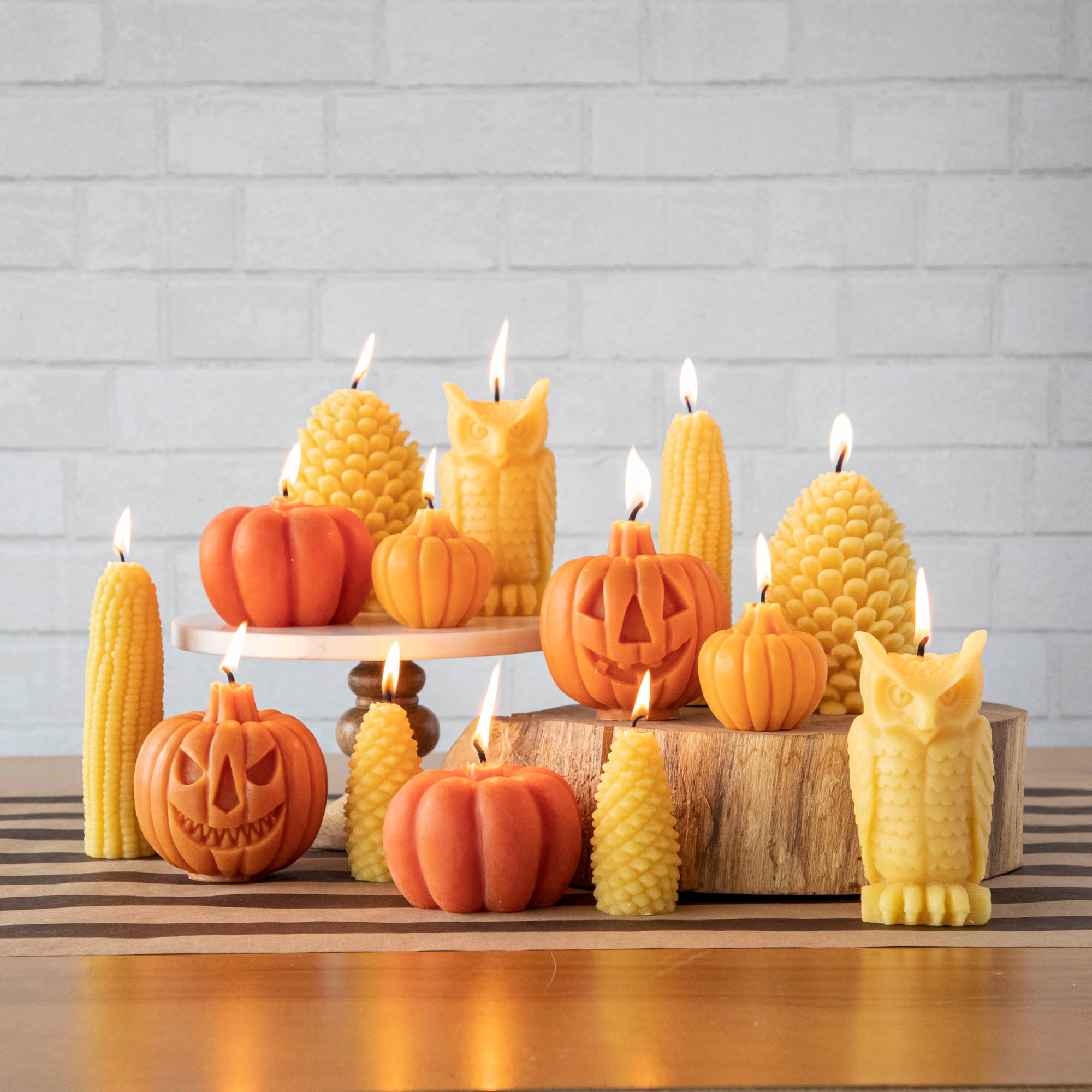 Corn, pumpkin, jack-o-lantern, owl and pinecone beeswax candles displayed on a table.