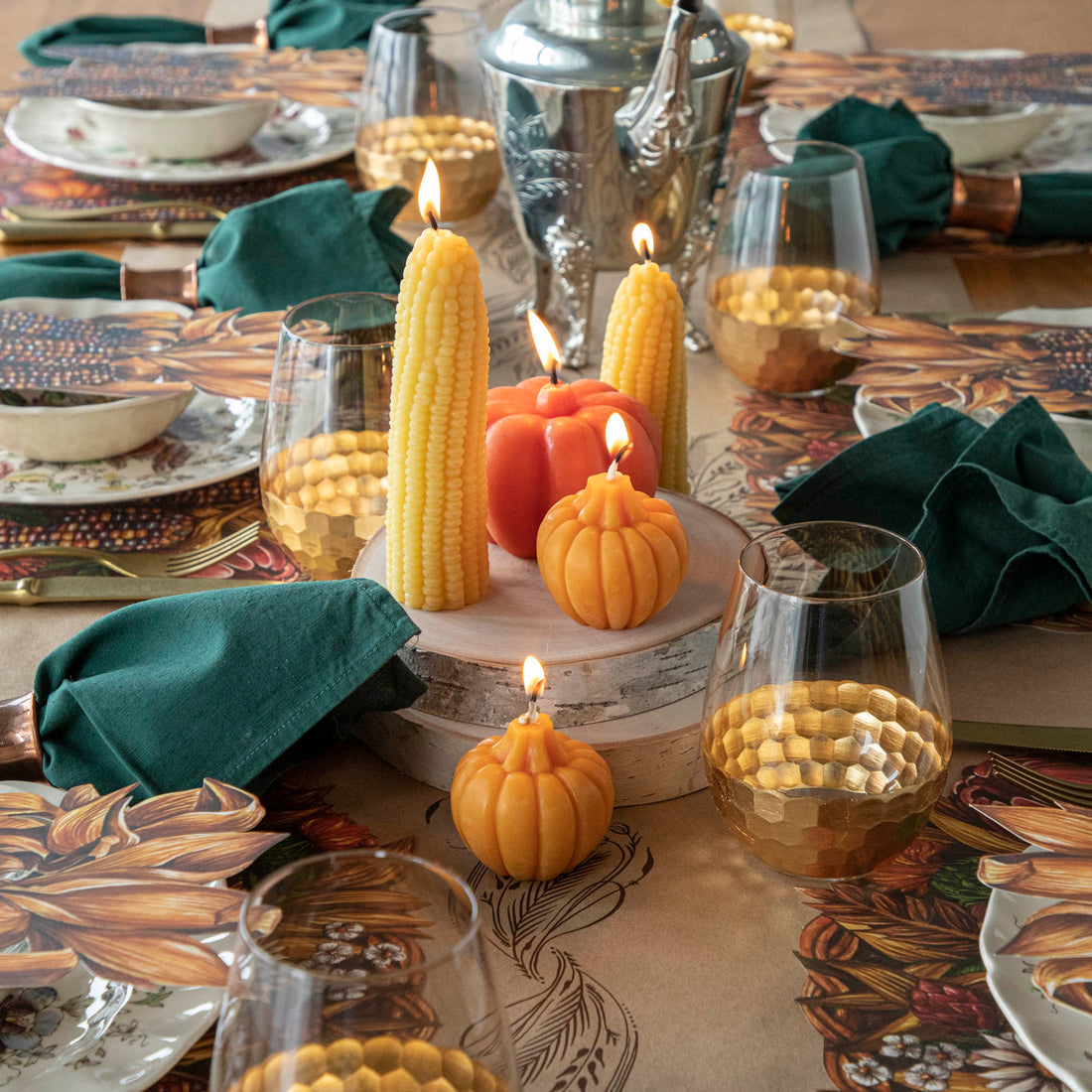 A collection of lit fall-themed candles on an elegant fall tablescape.  