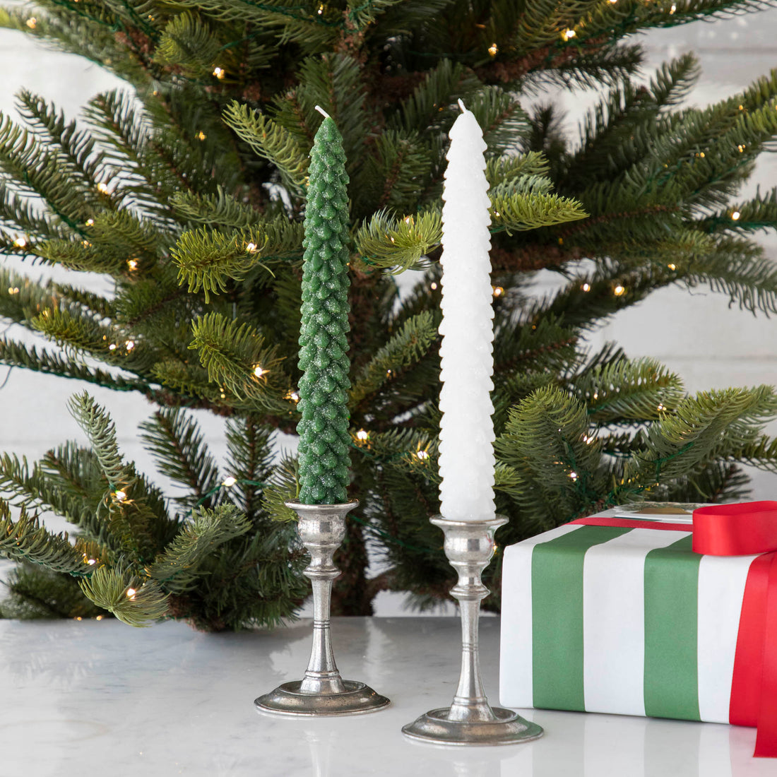 Two Glitterville Tree Shaped Taper Candles on a counter next to a Christmas tree.