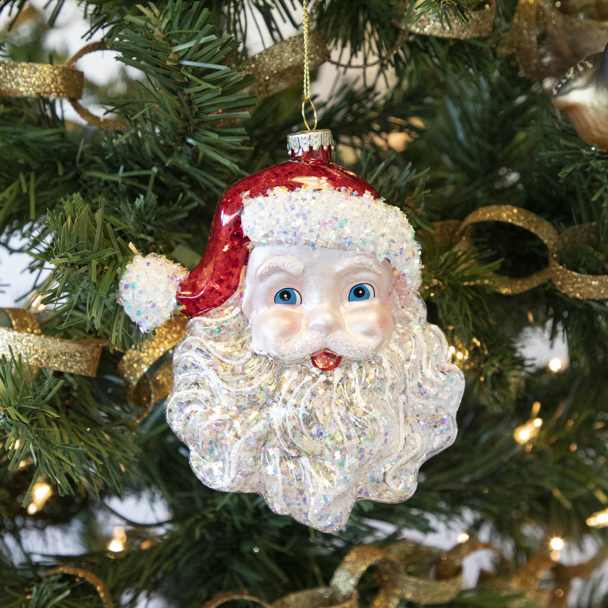 A Glitterville Glass Santa ornament, radiating festive cheer, hanging on a Christmas tree.