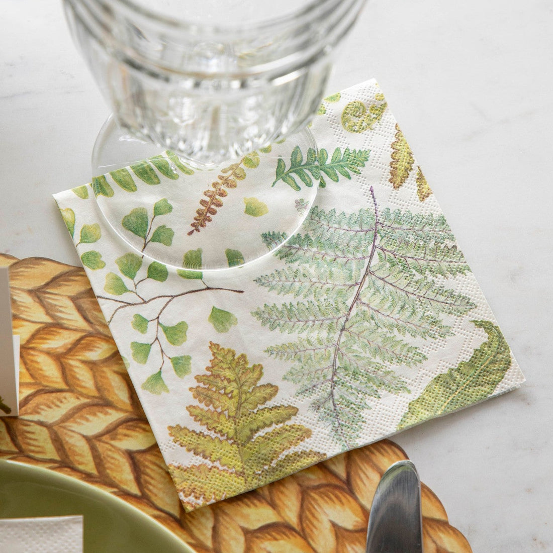 A Fern Cocktail napkin under a water glass, as part of an elegant place setting.