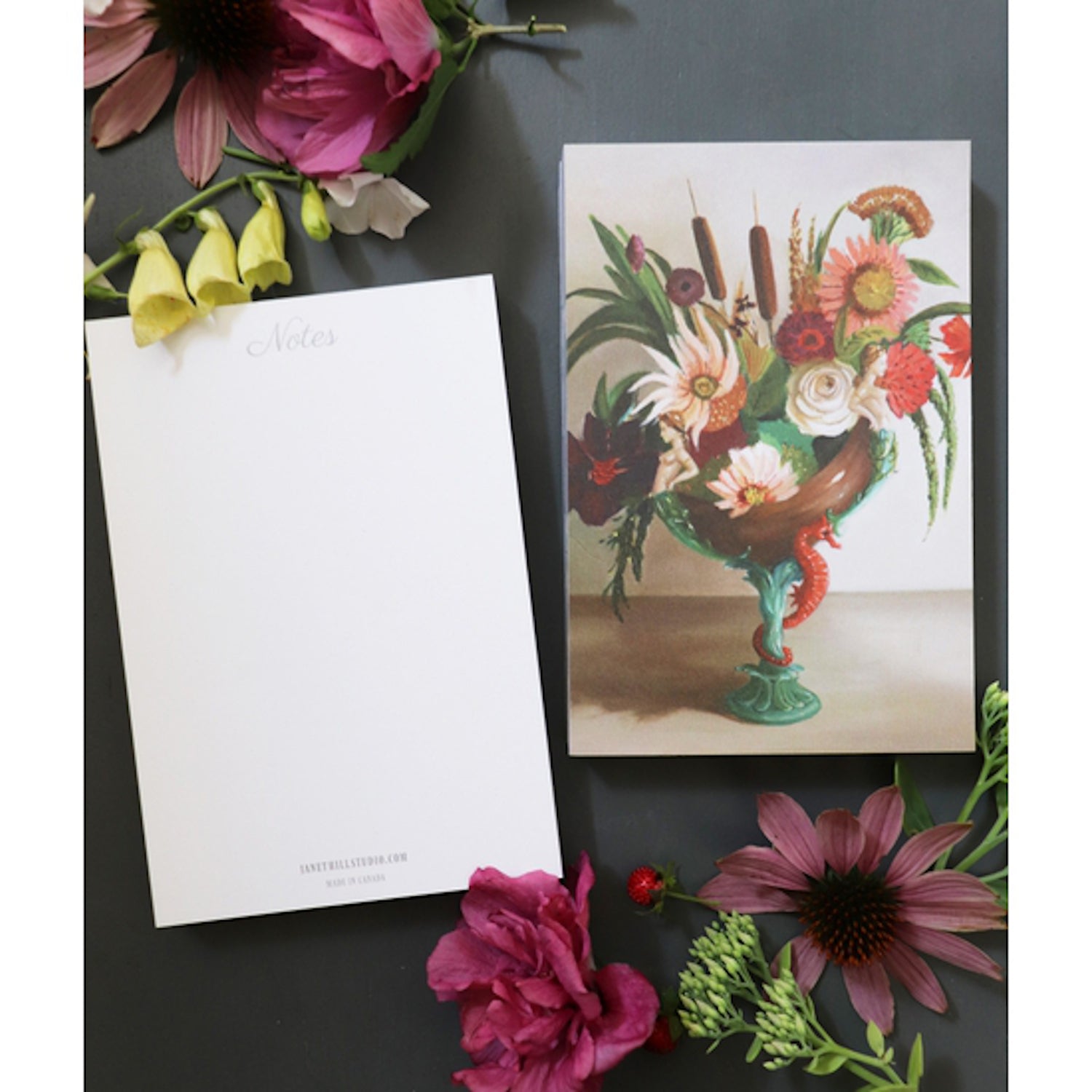 The &quot;Lost at Sea&quot; Tear-Away Notepad resting on a table with flowers, next to a single removed sheet flipped over to show the blank white back side labeled &quot;Notes&quot; at the top. The artwork is a painterly illustration of a bouquet of flowers and botanicals in an asymmetrical teal vase with an orange seahorse on the base, resting on a beige table.