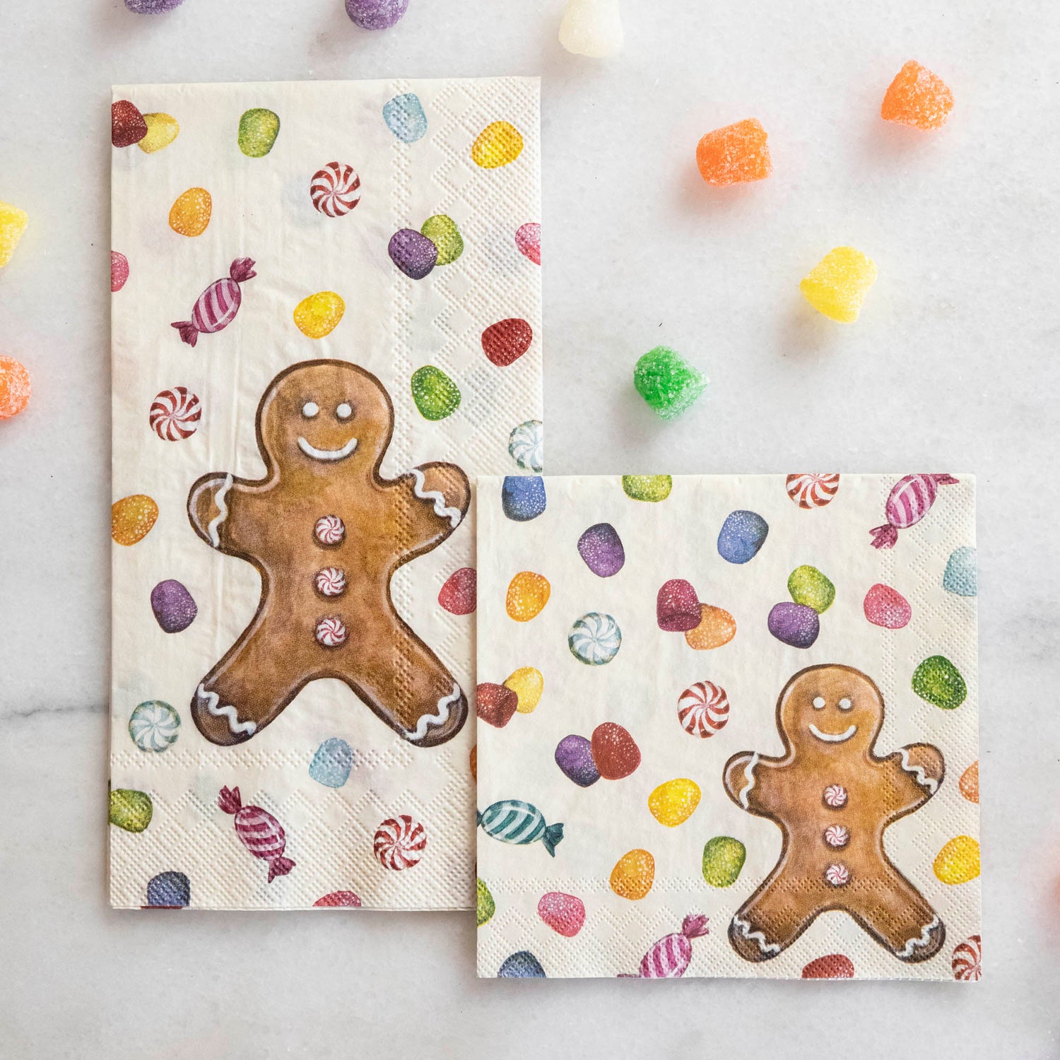 Two Gingerbread Napkins, one Guest and one Cocktail, on a white table surrounded by gumdrops.