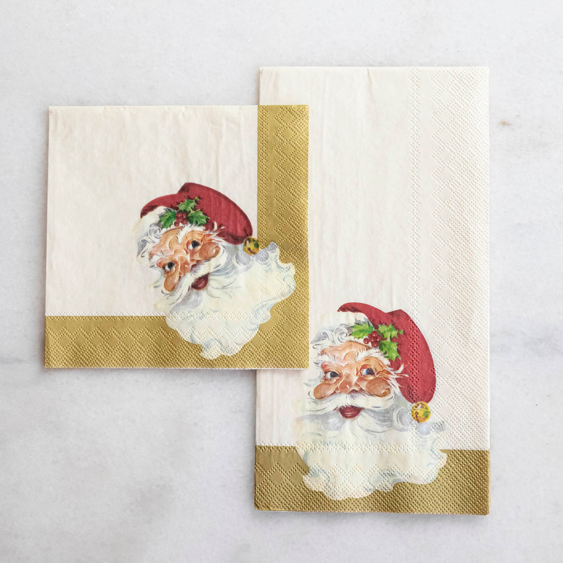 A Santa Cocktail Napkin overlapping a Santa Guest Napkin on a white table.