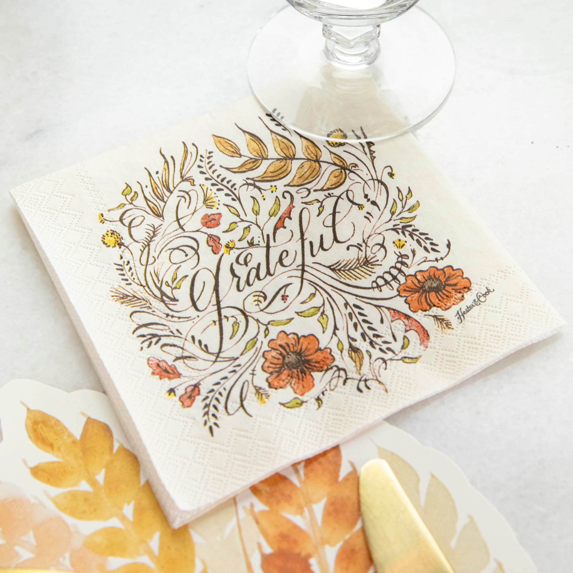 A Grateful Cocktail Napkin under a glass in an elegant Thanksgiving place setting.