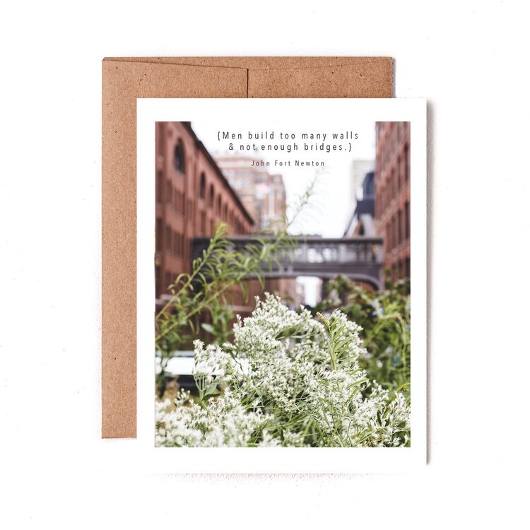 A Building Bridges greeting card by The Pen + Piper with a quote by John Petit-Senn on an urban background, presented on a white surface with an accompanying kraft envelope.