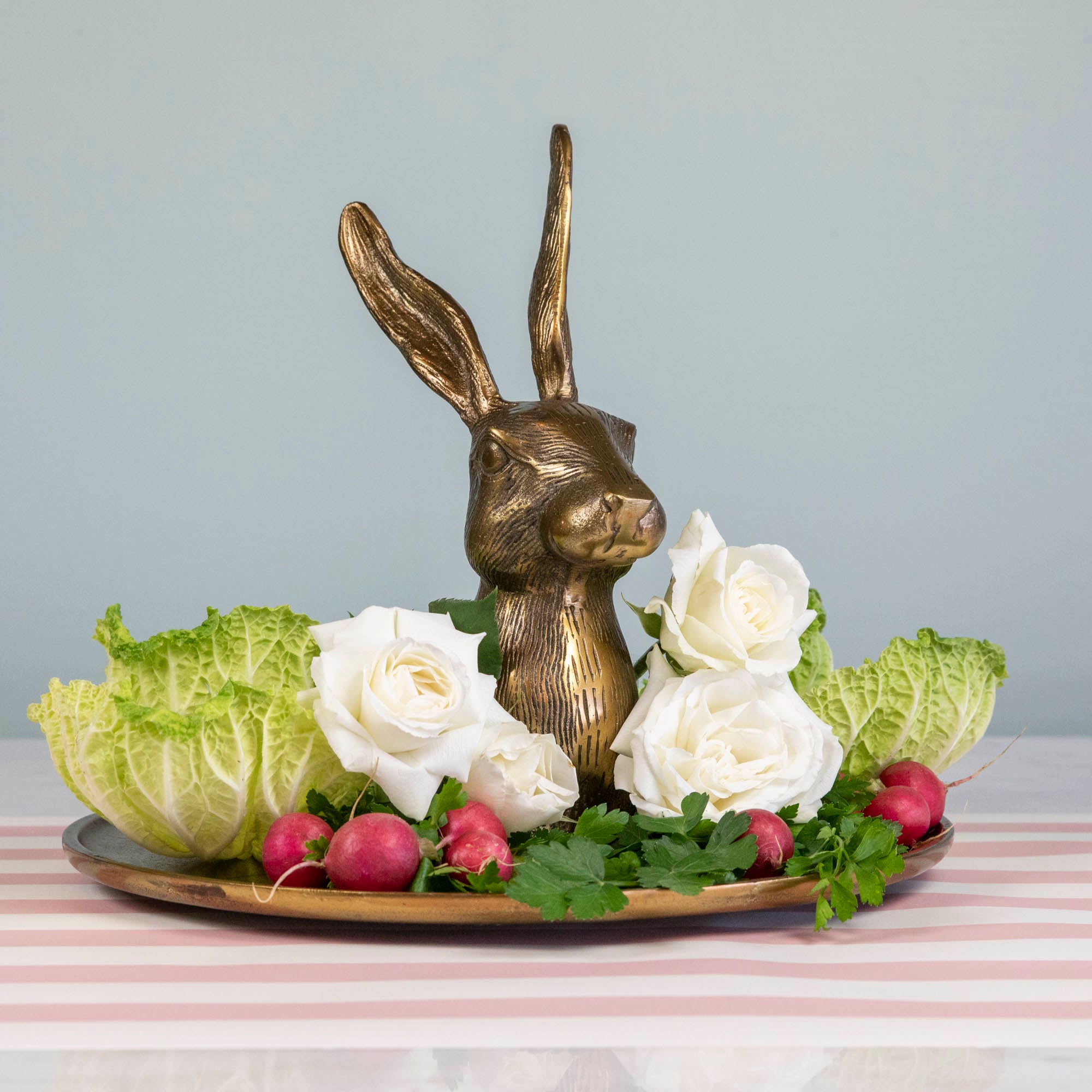A whimsical Hare Platter from Accent Decor, featuring a gold bunny head with radishes and flowers, on a table.