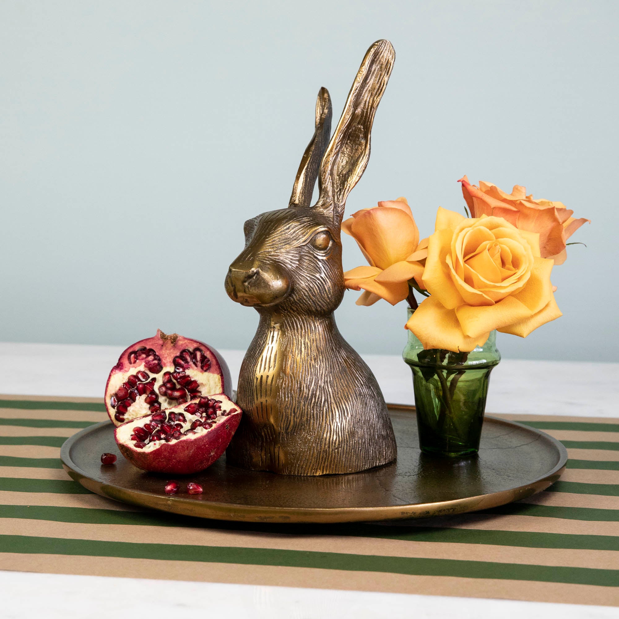 A whimsical gold rabbit sits on an Accent Decor Hare Platter adorned with flowers and pomegranate, placed on a table.