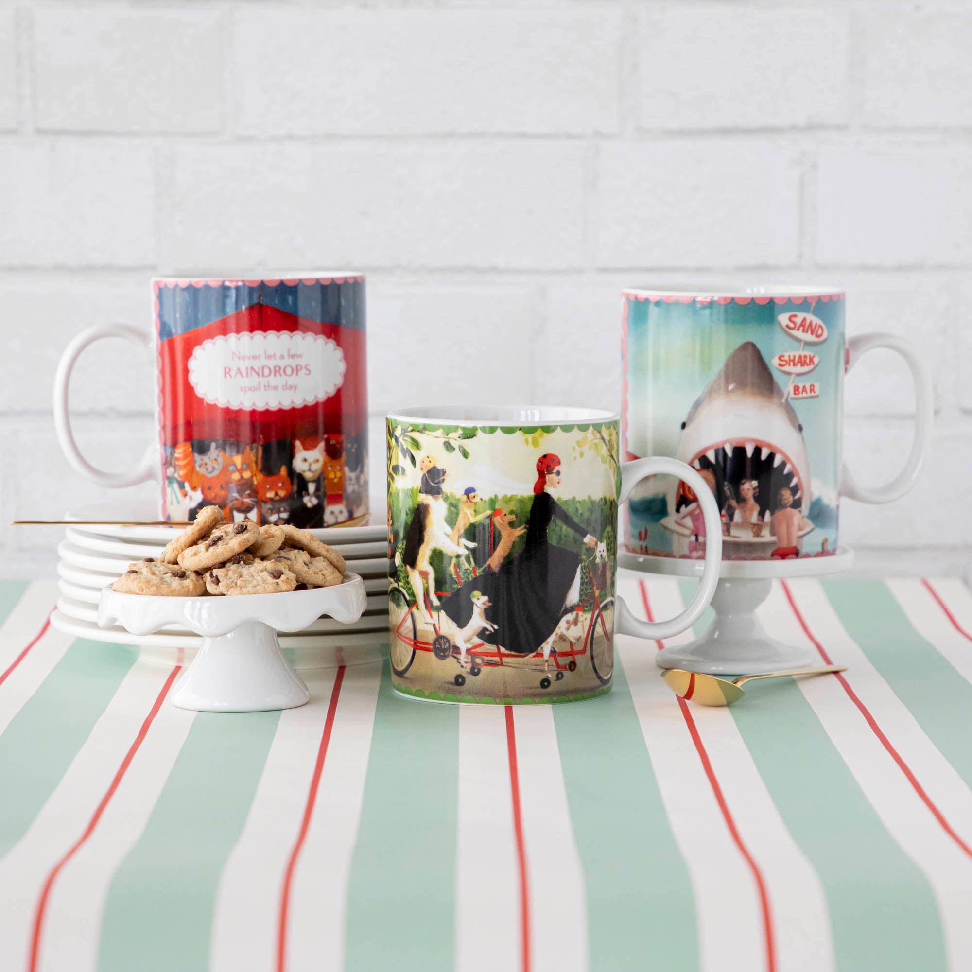 Three New York Puzzle Company Shark Bar Mugs on a table with cookies and crackers.