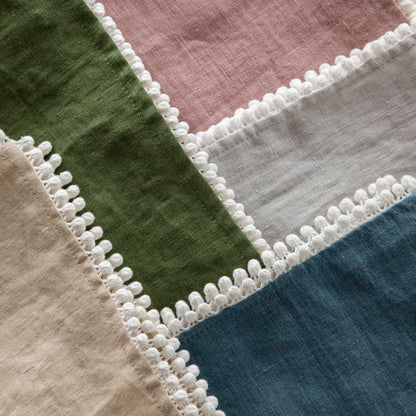Assorted European Spring Napkin Collection with pom-pom trim edges displayed on a marble surface by Magic Linen.