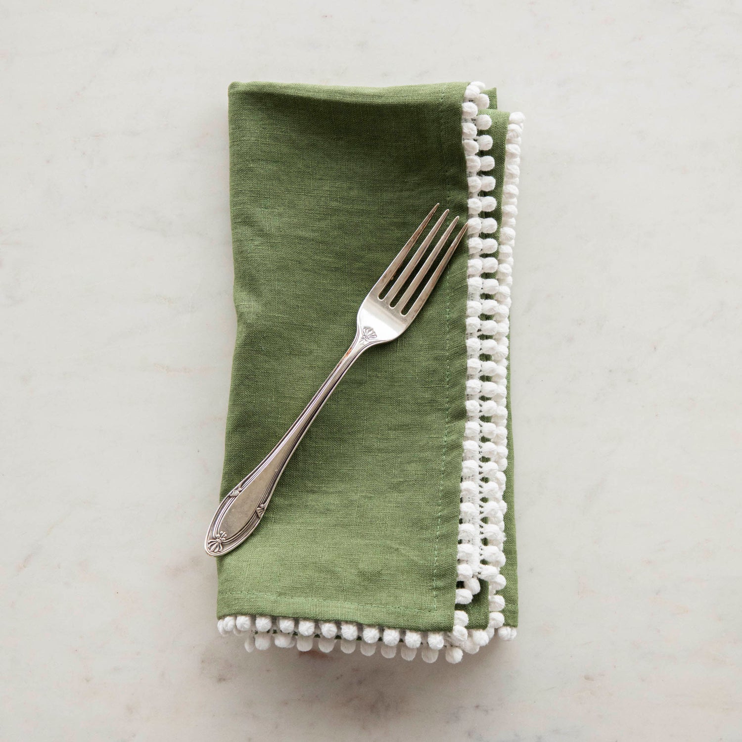 Assorted European Spring Napkin Collection with pom-pom trim edges displayed on a marble surface by Magic Linen.
