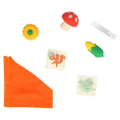 An orange tissue paper party hat, a sticker with a fox holding an acorn, a sticker of a maple leaf,  a  joke and three different erasers; a mushroom, a corn, and a pumpkin 