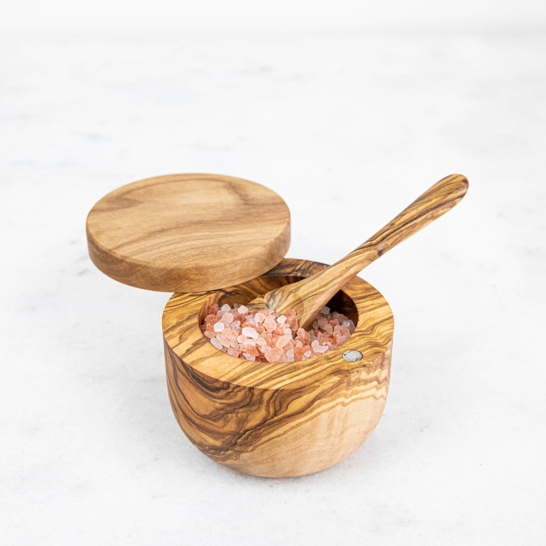 An Natural Olivewood olive wood salt cellar with a spoon, containing pink Himalayan salt. Hand wash only.