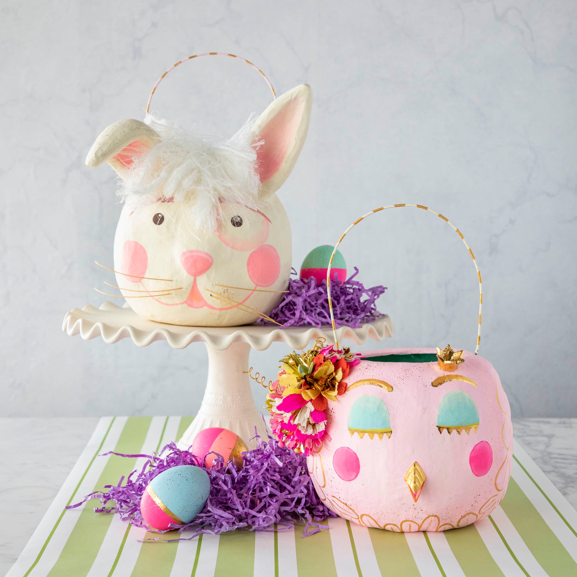 Two Glitterville Papermache Easter Buckets decorated with bunnies and easter eggs, perfect for Easter fun and spring decor.