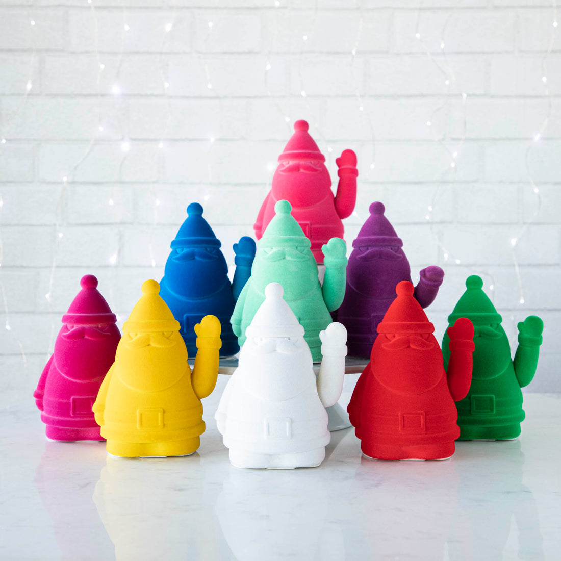 A group of colorful, Glitterville Waving Flocked Santa figurines on a table.