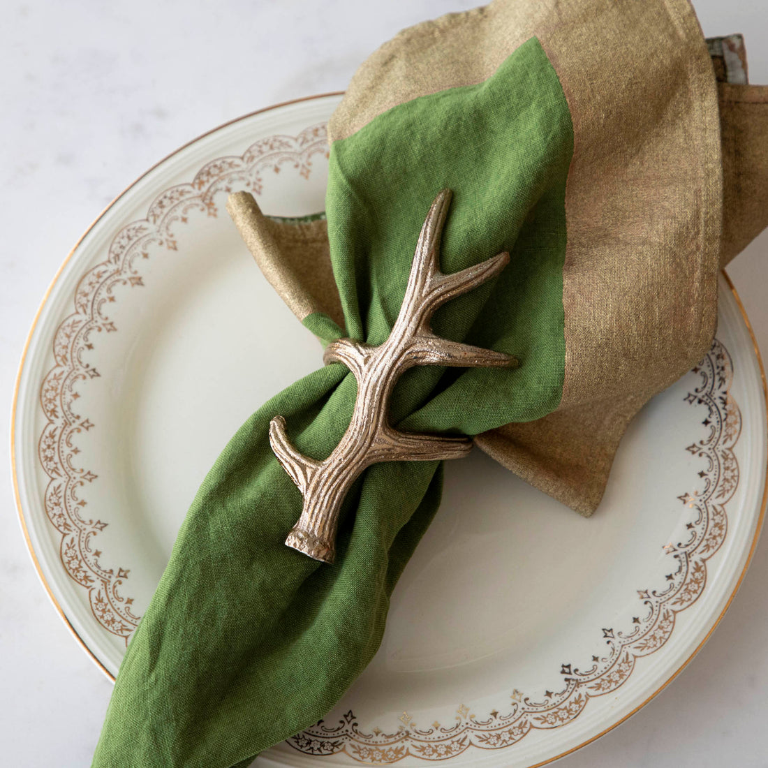A napkin ring featuring an antler design, placed on a white plate with a green napkin inserted.
