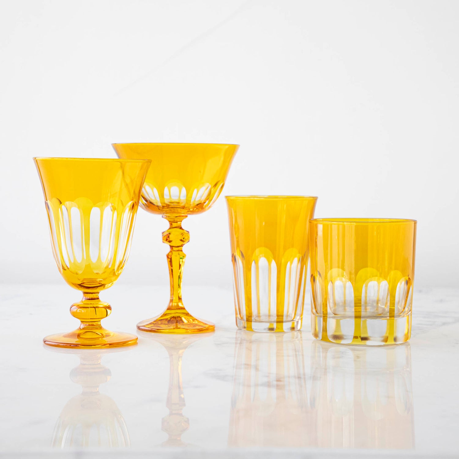 A set of Rialto Ginger (Dark Yellow) glasses from SIR/MADAM on a white surface, including two stemmed glasses and two tumblers with a vertical line pattern.