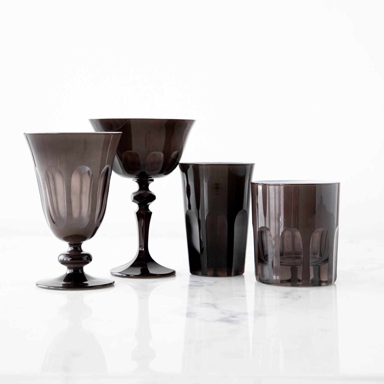 A set of three SIR/MADAM Rialto Warm Gray Glasses of varying styles on a marble surface.