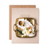 A top-down photo of a gold tray on a tan background, with a white cup of hot cocoa, a white plate of macaroons and white rose blooms, "{showering you with lots of love}" printed above the tray.